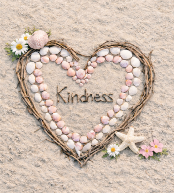 Close-up of a heart created from scallop shells of varying sizes, surrounded by driftwood, grapevine, and wildflowers, arranged on sandy beach.